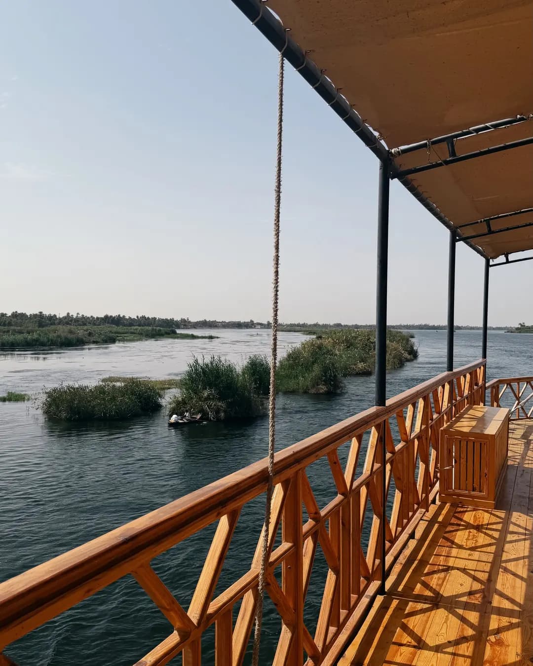 Le pont abrité d'un bateau et sa rambarde en bois, face au Nil