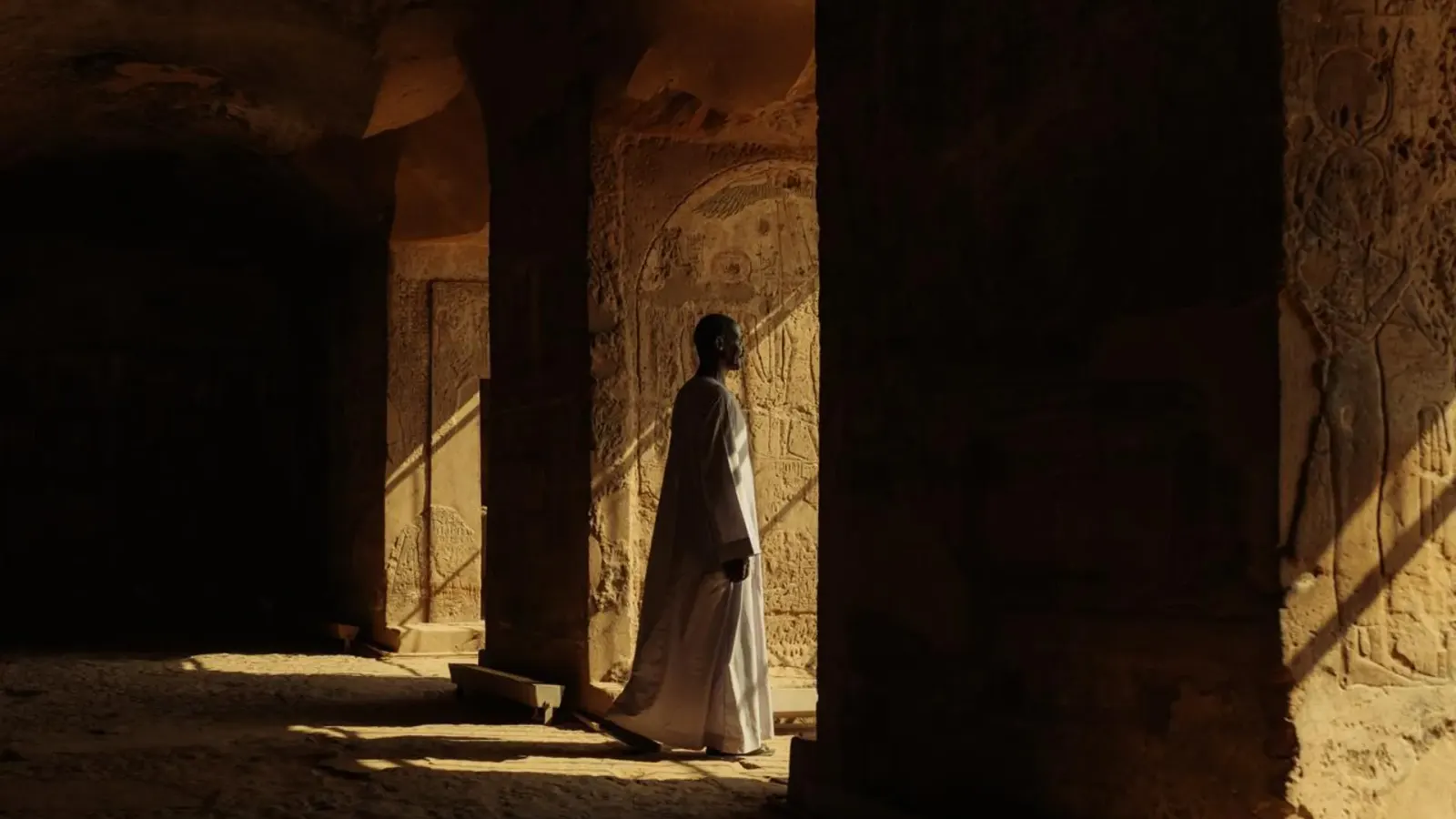 Un Égyptien en galabeya traditionnelle dans un temple baigné de lumière dorée