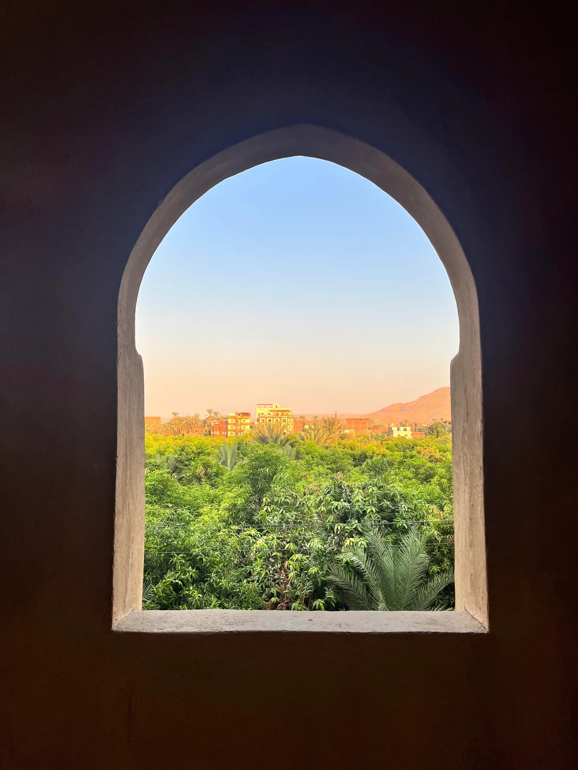 Fenêtre en arche ouverte sur la palmeraie de Louxor au crépuscule